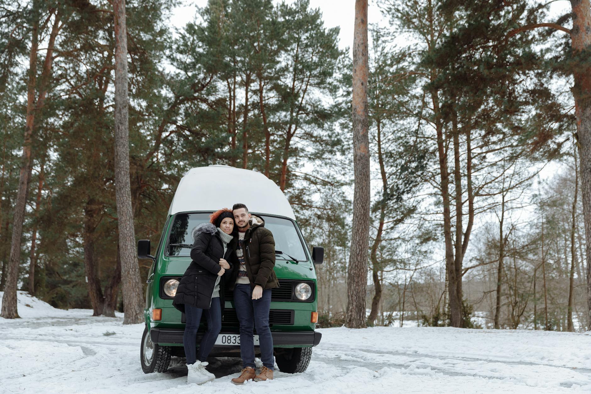 couple in front of a green van while in the forest